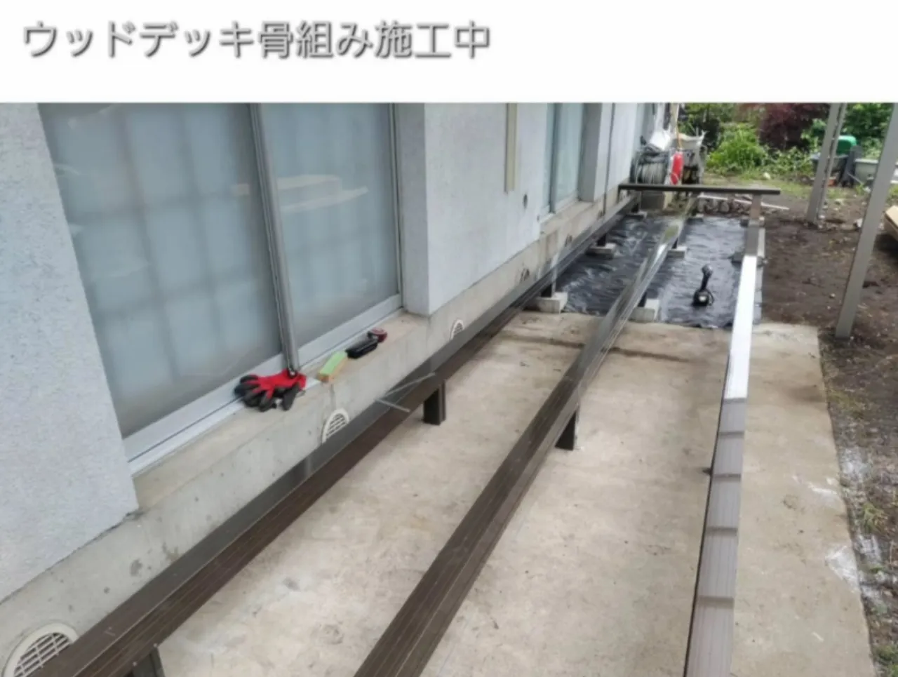 防草シートと基礎石を据え付けLIXIL樹ら楽ステージの骨組みを組んでいる施工中の写真。既存犬走りを基礎として活用した中之条町のデッキ新設工程。